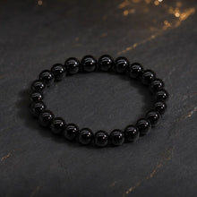 Bracelet en agate noire à perles rondes polies sur fond sombre aux reflets dorés