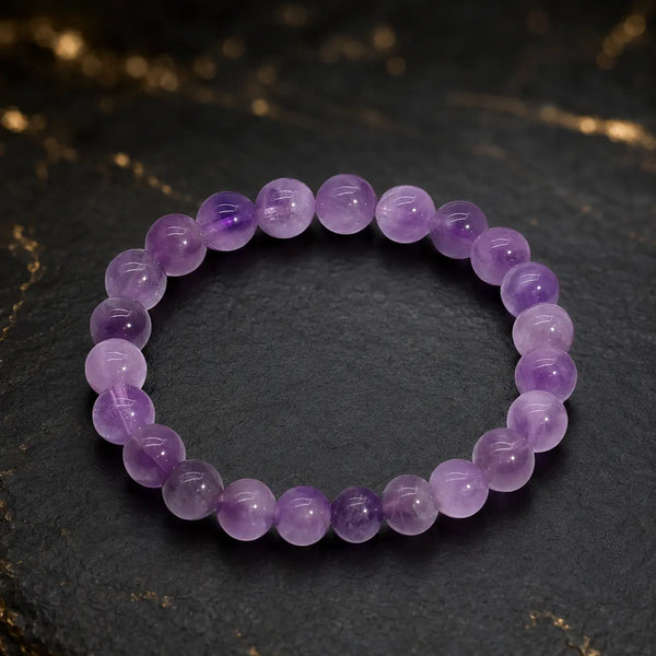 Bracelet en améthyste à perles violettes polies sur fond sombre aux détails dorés