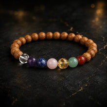 Bracelet en bois de cèdre avec sept perles chakra colorées sur fond sombre aux reflets dorés
