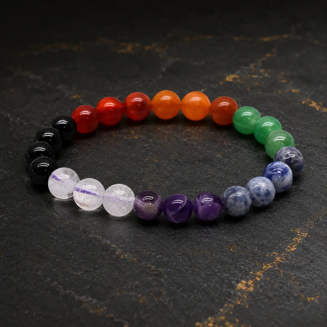 Bracelet en pierres des sept chakras aux perles multicolores sur fond sombre et doré