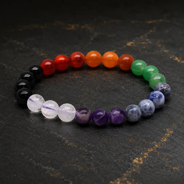 Bracelet en pierres des sept chakras aux perles multicolores sur fond sombre et doré