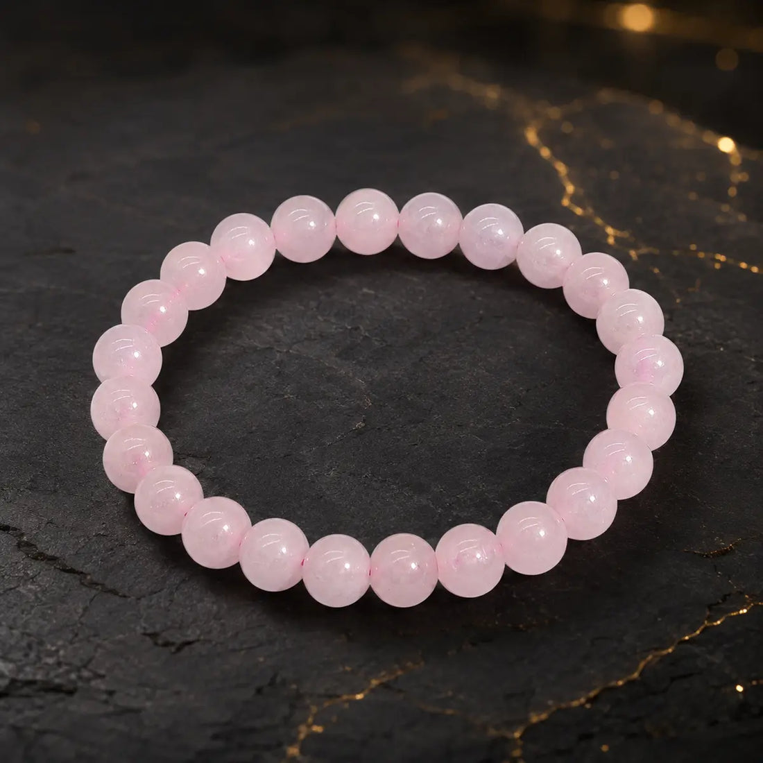 Bracelet en quartz rose à perles roses translucides sur fond sombre aux reflets dorés